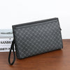 A black leather wallet or clutch with a diagonal pattern and a black strap resting on a wooden surface.