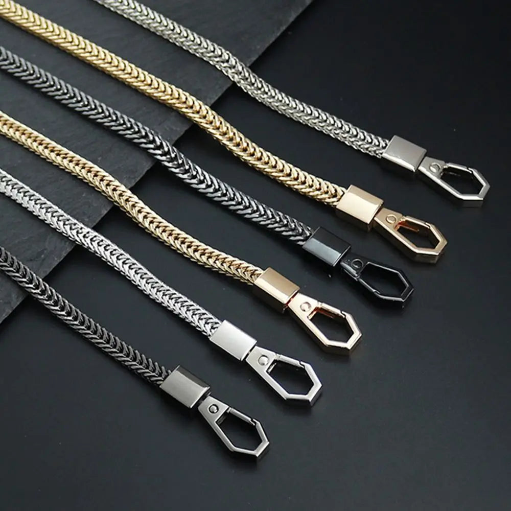 Multiple metal bag chain straps in silver and gold tones laid out on a dark surface.