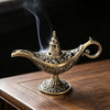 Antique metal incense burner with a spout and handle emitting smoke on a wooden surface.