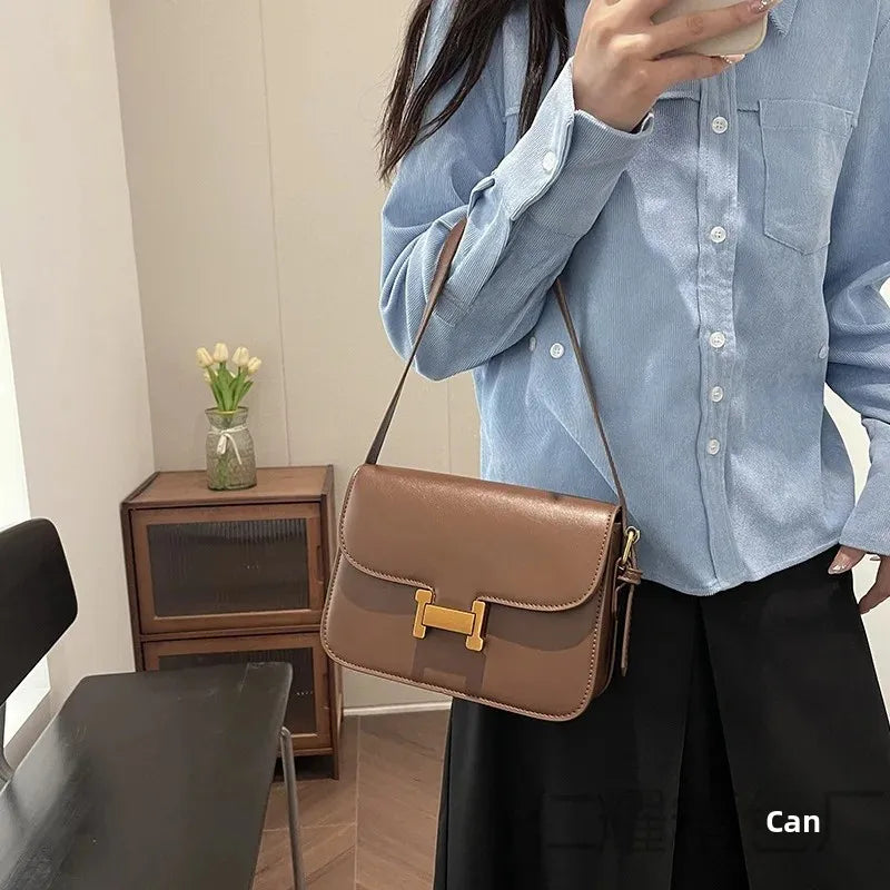 Eine Frau in blauem Shirt und schwarzen Hosen hält eine braune Ledertasche über eine Schulter.