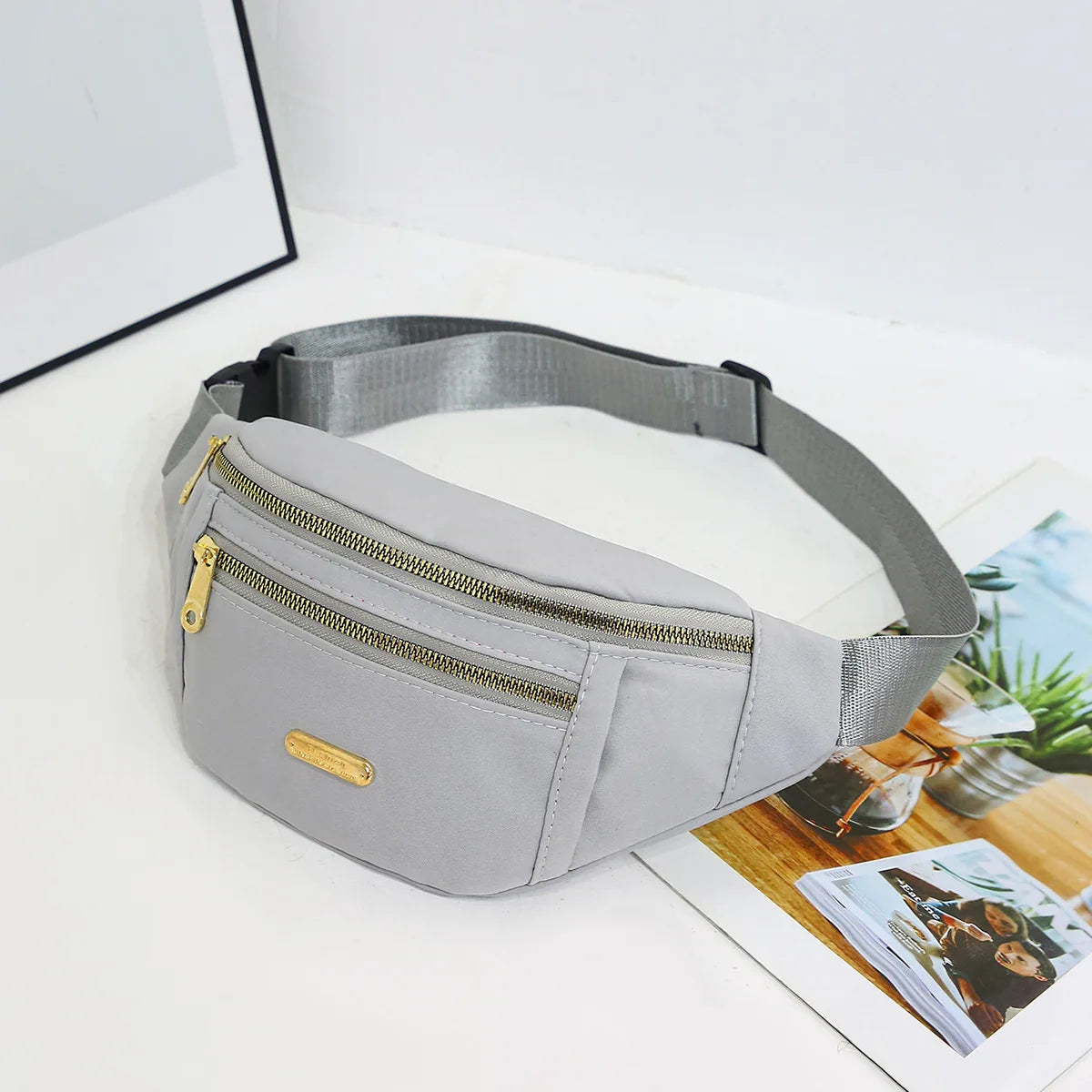 A light gray nylon crossbody fanny pack is shown lying on a white surface.