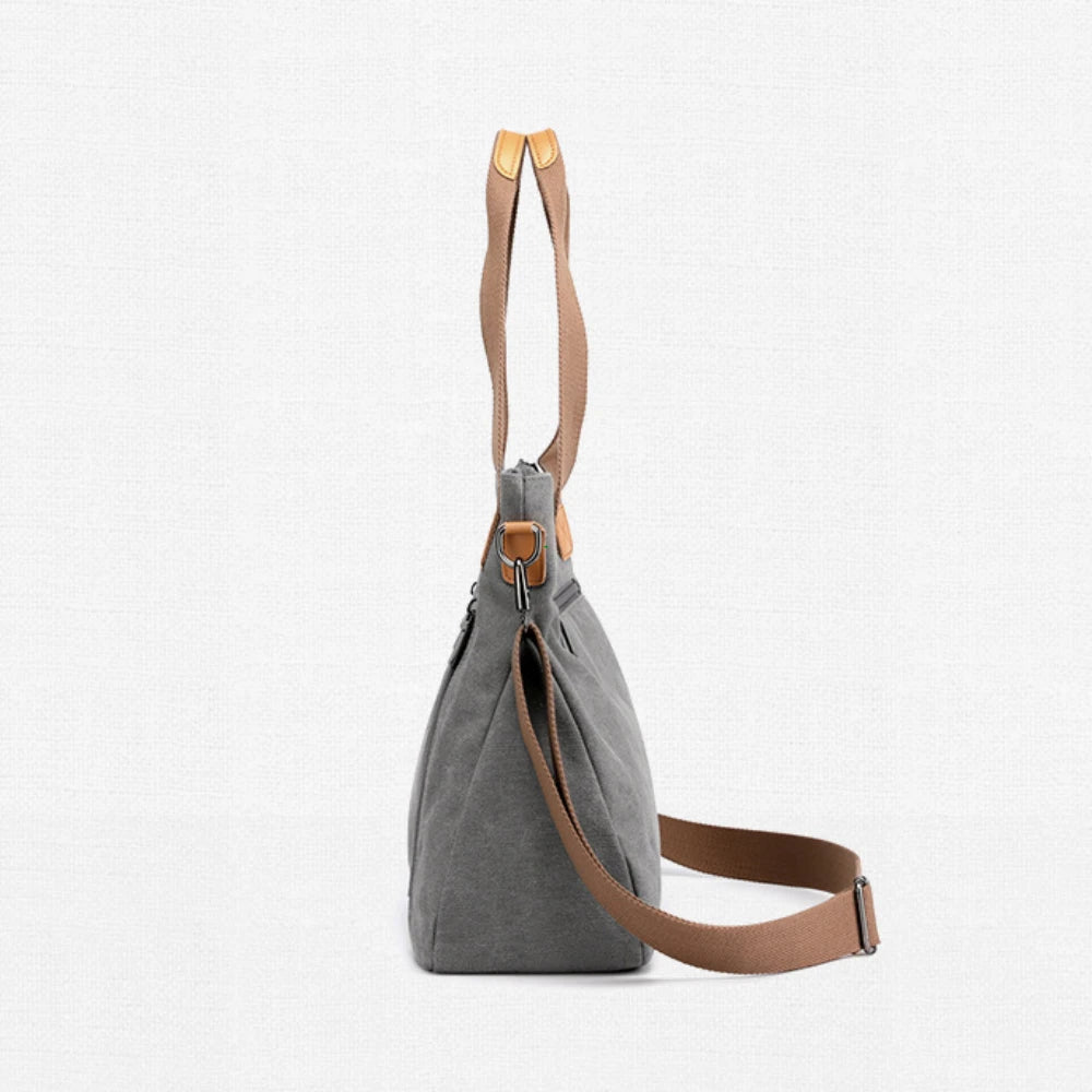 A grey canvas tote bag with tan leather straps is shown against a white background.