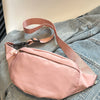 A light pink nylon crossbody sling bag with a tan strap resting on a denim jacket.