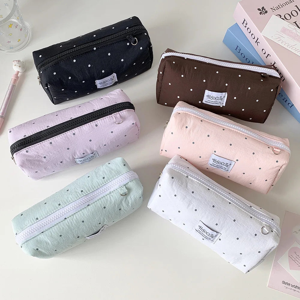 Eine Kollektion weicher Stoff-Pencil-Cases in verschiedenen Farben, darunter Schwarz, Pink, Braun und weiß mit Polka Dots.