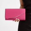 A bright pink velvet evening clutch with a silver detachable shoulder strap being held by a person.