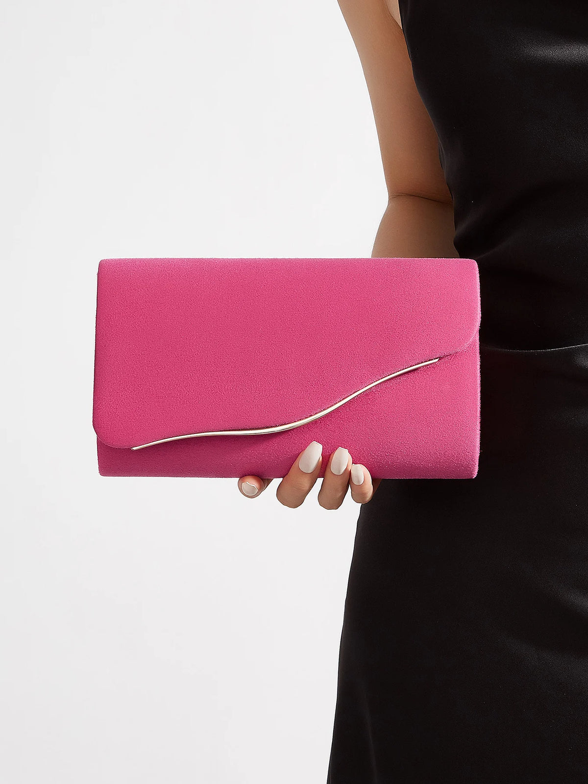 A bright pink velvet evening clutch with a silver detachable shoulder strap being held by a person.