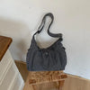 A gray plaid nylon drawstring tote bag resting on a wooden surface against a white wall.