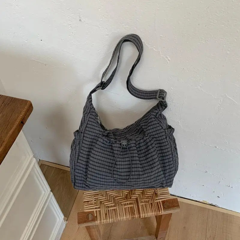 A gray plaid nylon drawstring tote bag resting on a wooden surface against a white wall.