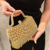 A hand holds an elegant gold diamond rhinestone evening clutch bag with a golden tassel against a black background.
