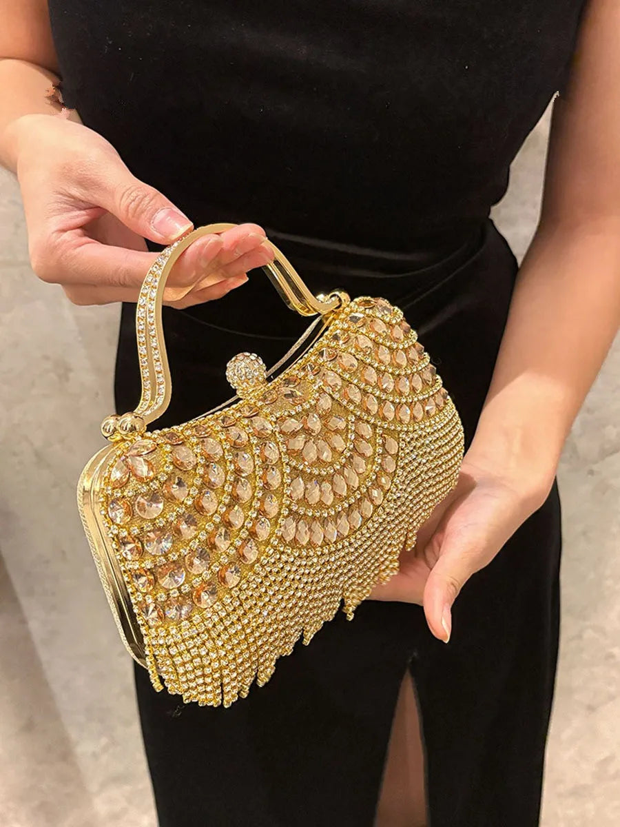 A hand holds an elegant gold diamond rhinestone evening clutch bag with a golden tassel against a black background.