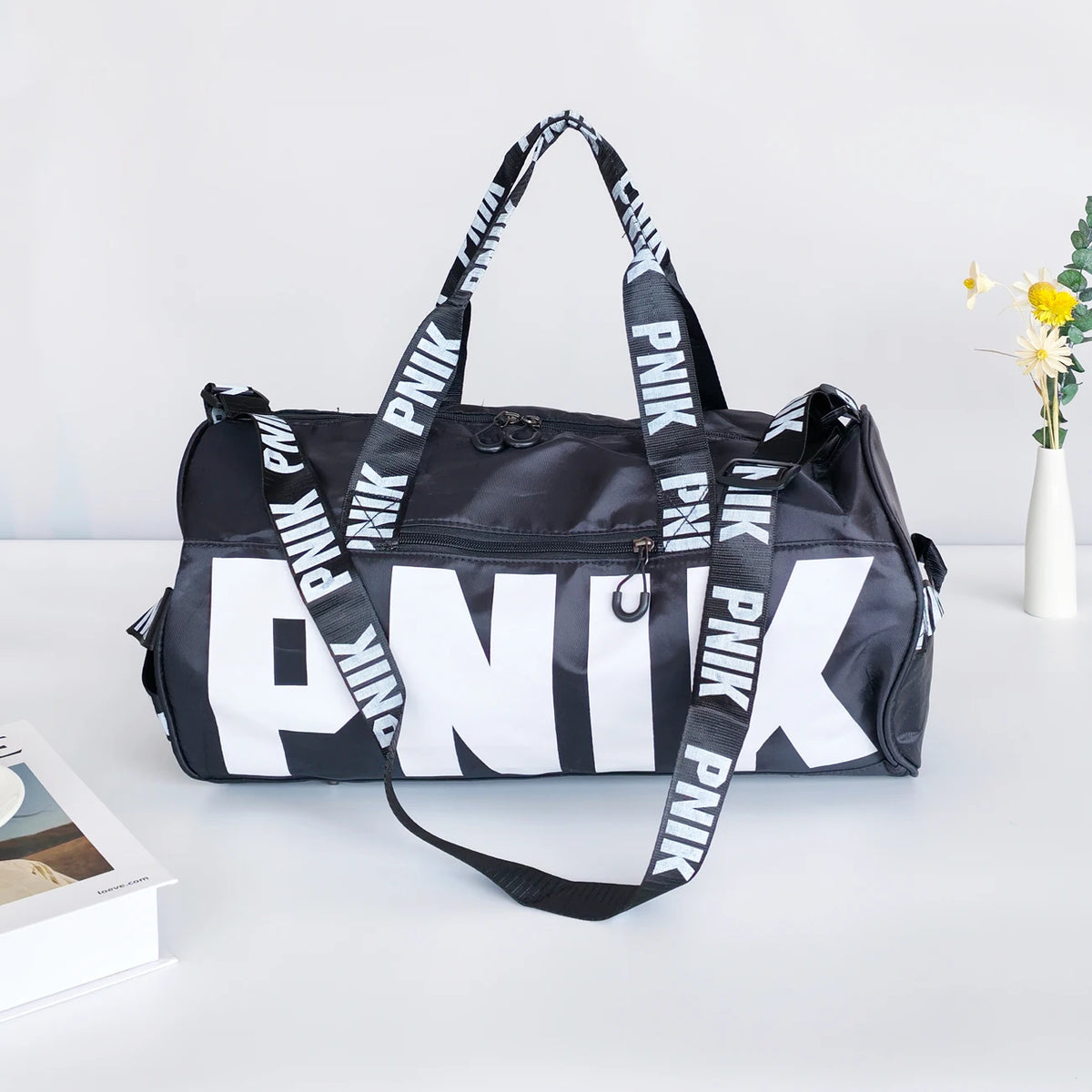A black and white printed shoulder bag with black straps is displayed on a white surface.
