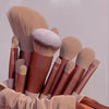 Una colección de trece brochas de maquillaje profesionales en varios tonos y tamaños, apoyadas sobre un tejido drapeado.