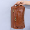 Braune Vintage-PU-Leder-Toiletten-Tasche mit Reißverschluss und Aufhänger, gehalten von einer Hand.