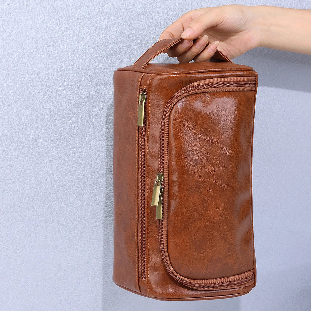 Braune Vintage-PU-Leder-Toiletten-Tasche mit Reißverschluss und Aufhänger, gehalten von einer Hand.