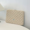 Funda acolchada beige para portátil con sutil patrón floral sobre una superficie blanca.