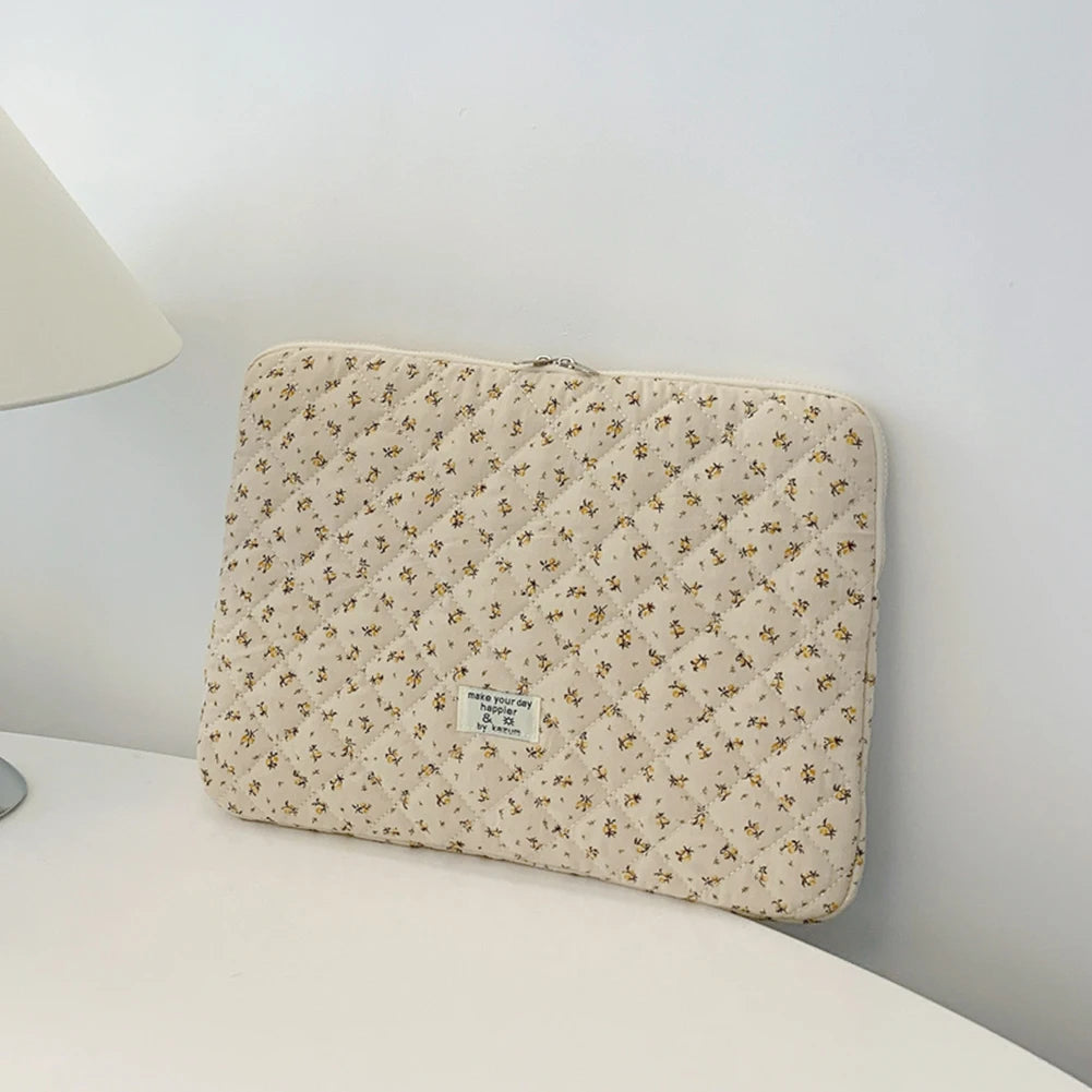 Funda acolchada beige para portátil con sutil patrón floral sobre una superficie blanca.