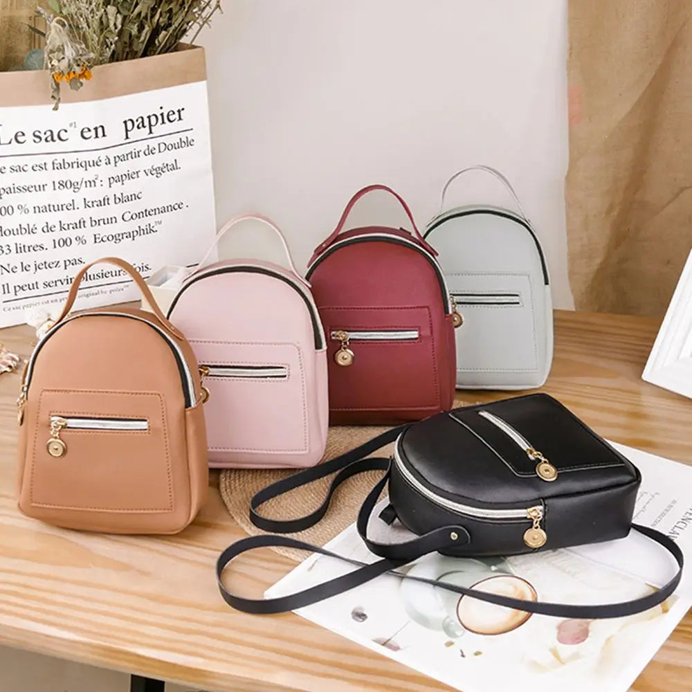 A pink mini backpack and a black leather clutch are displayed on a wooden table.