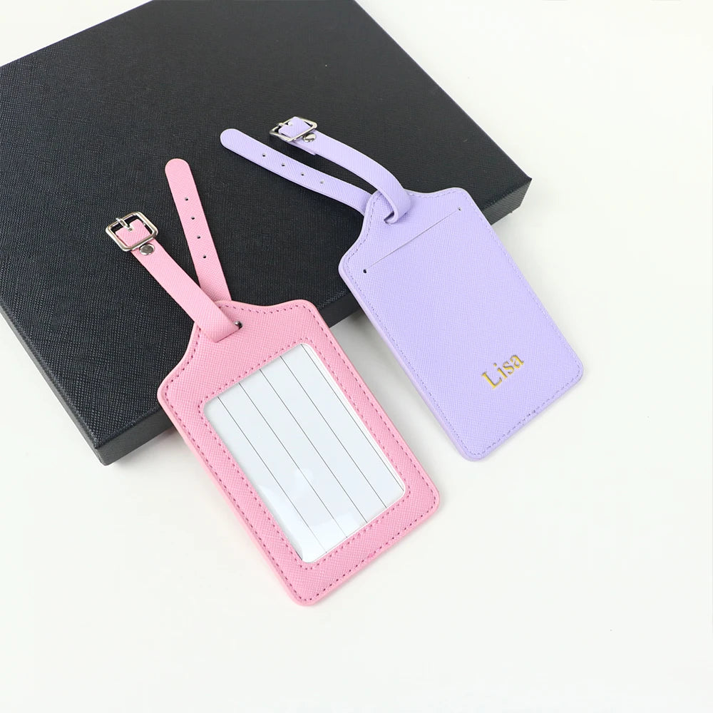 A set of two custom PU leather luggage tags, one pink and one purple, with a cross-pattern detail.