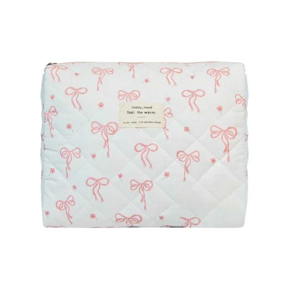 A light blue quilted cosmetic bag with pink ribbon embroidery and a tag reading today mood feel the warm.