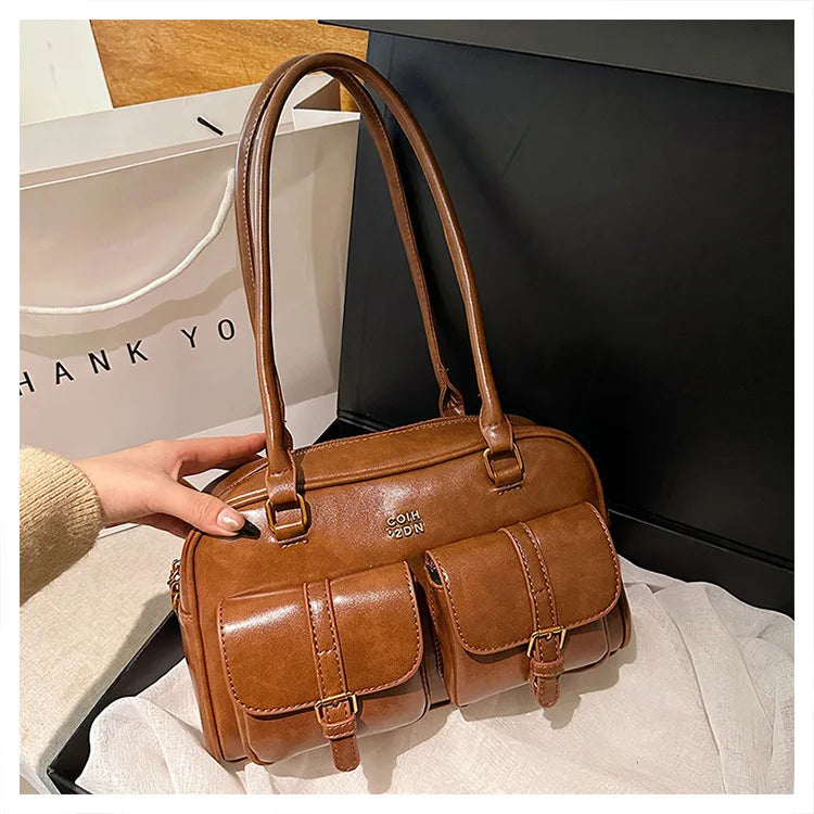 Bolso de hombro retro de cuero PU marrón con asas de cuero sobre una tela clara.