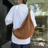 A person wearing a white shirt and dark pants is holding a brown corduroy casual crossbody shoulder bag.