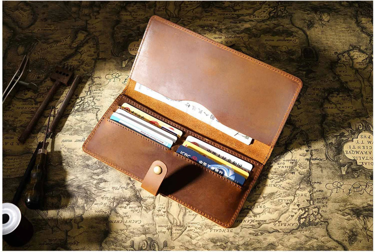 A brown genuine leather long bi-fold wallet with a snap closure resting on an old map.