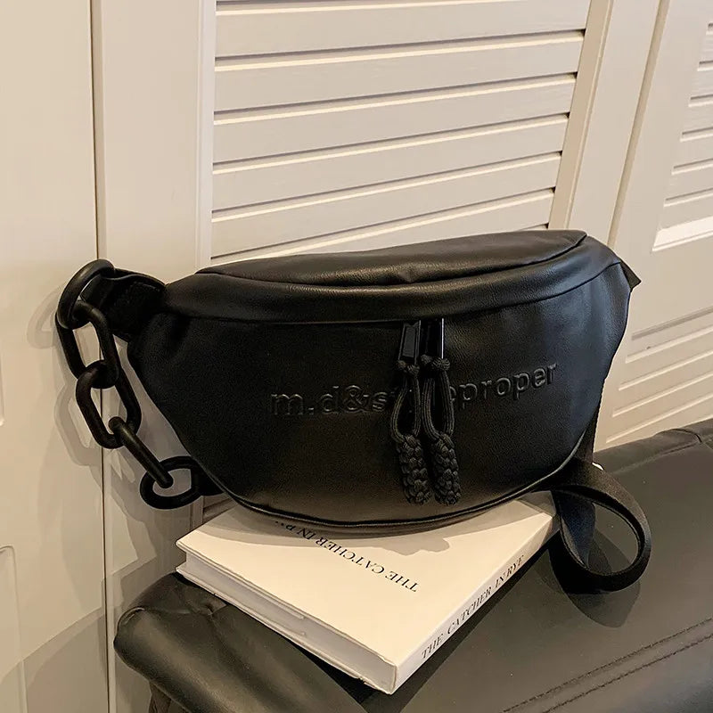 Black m.d&s proper leather crossbody saddle bag with a chain strap resting on a white book.