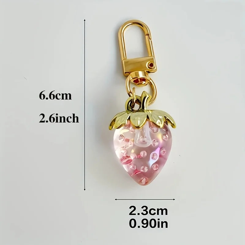 Gold-toned keychain featuring a clear pink strawberry charm and a small cherry bag charm.
