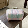A hand woven PVC vegetable basket tote bag with pink, green, and white stripes resting on a wooden table.