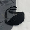 A black nylon crossbody sling bag is shown resting on a gray blazer or jacket.