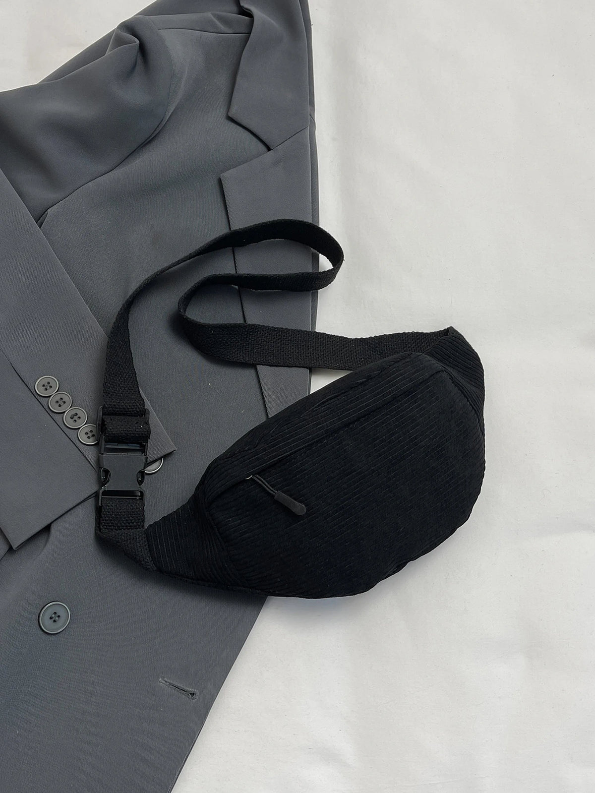A black nylon crossbody sling bag is shown resting on a gray blazer or jacket.