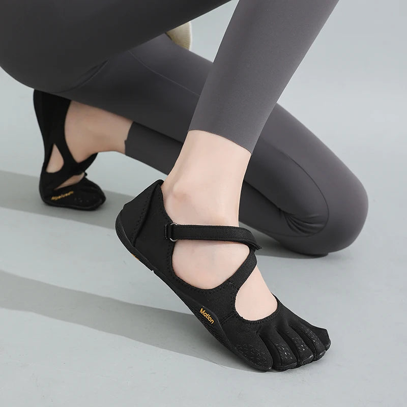 A pair of black women's barefoot five-toe shoes with an adjustable strap shown on a person's foot.
