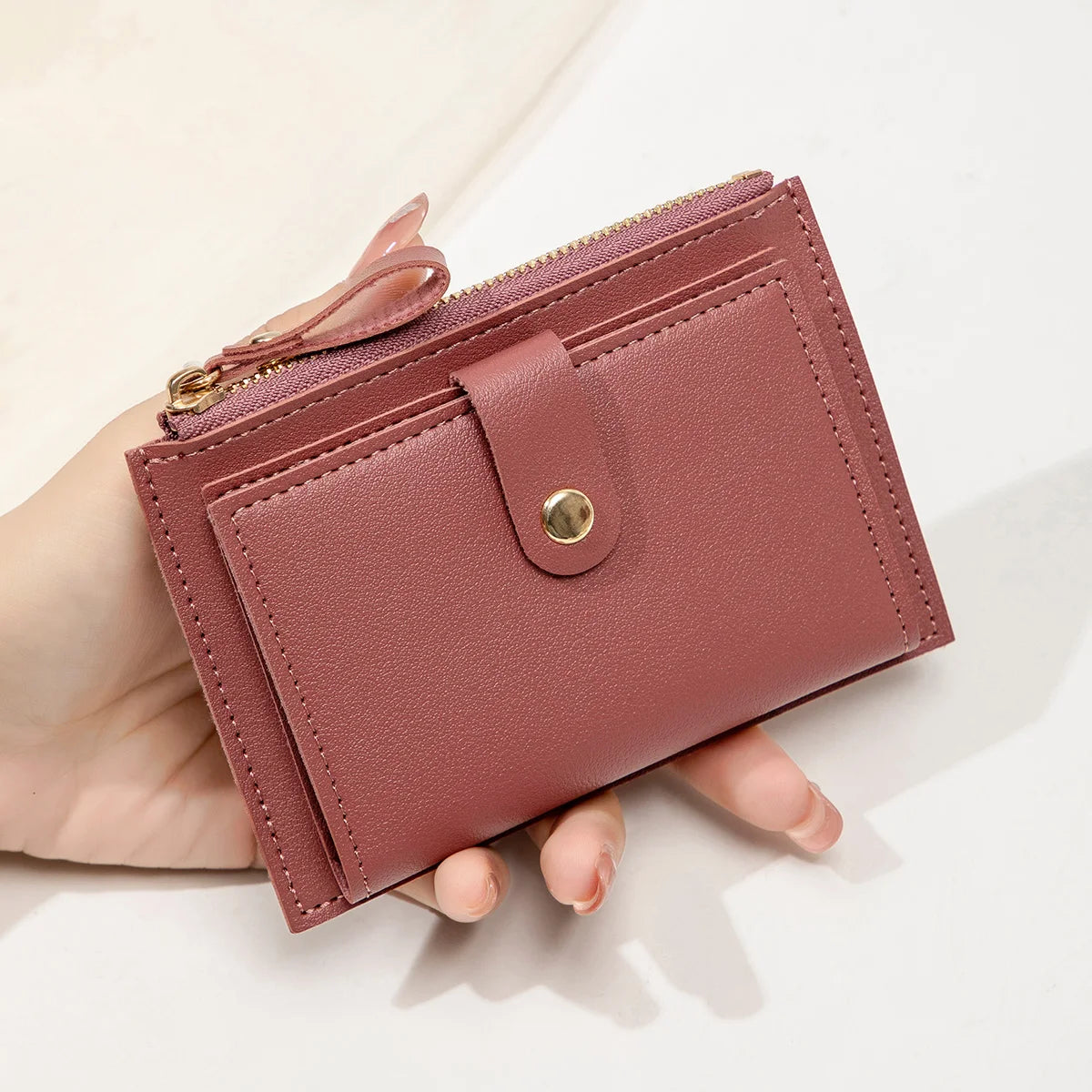 A hand holds a mauve pink ultra-thin PU leather card holder wallet with a zipper closure.