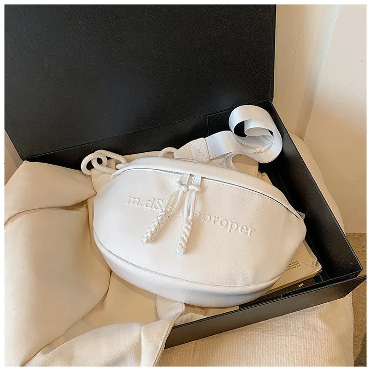 A white PU leather crossbody saddle bag with a chain strap is displayed inside a black box.