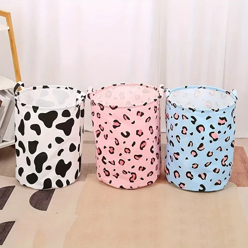 Trois paniers à linge en tissu à imprimé léopard noir, rose et bleu, posés sur un tapis clair.