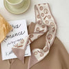 Un foulard de cheveux en soie beige avec des motifs de visages souriants, drapé à côté d'un carnet et d'une tasse à thé.