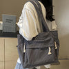Sac cabas en velours côtelé gris avec plusieurs poches, vu de dos, porté par-dessus un t-shirt blanc.
