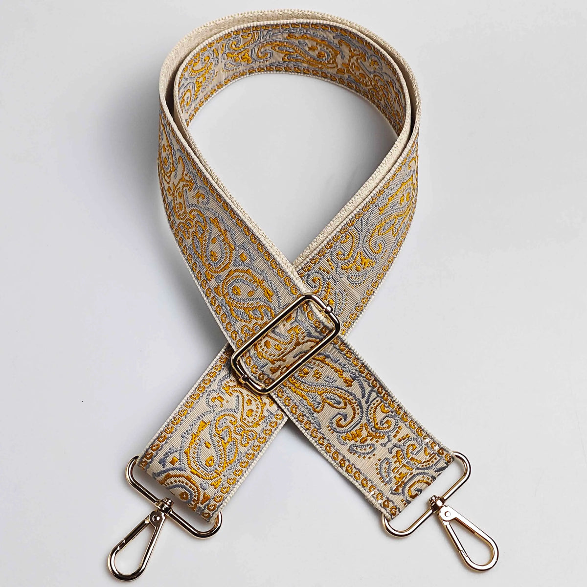 Correa ajustable de bolso cruz con patrón beige y dorado y hebilla plateada.