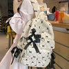 A woman holds a white backpack with black bow print details in a light pink dress.