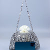 A handmade silver and gold beaded dumpling bag with a white bow, displayed above a dark blue smartphone.