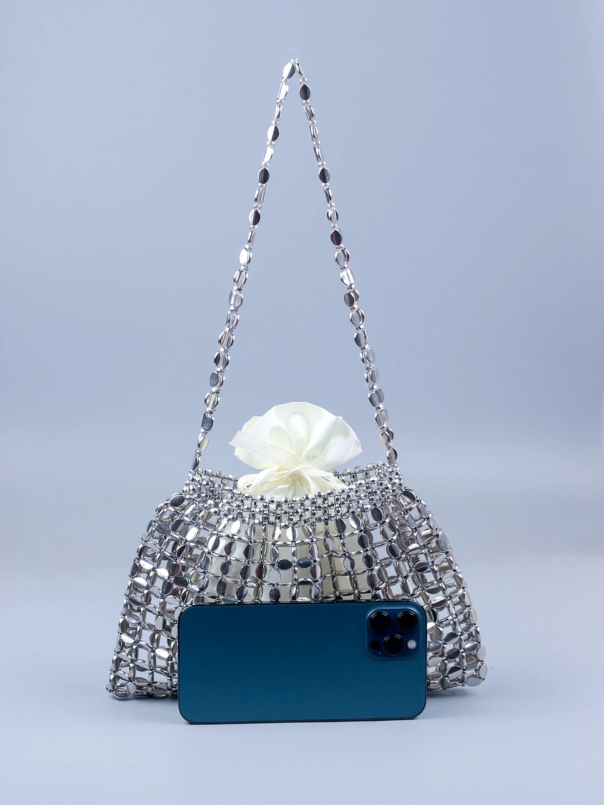 A handmade silver and gold beaded dumpling bag with a white bow, displayed above a dark blue smartphone.