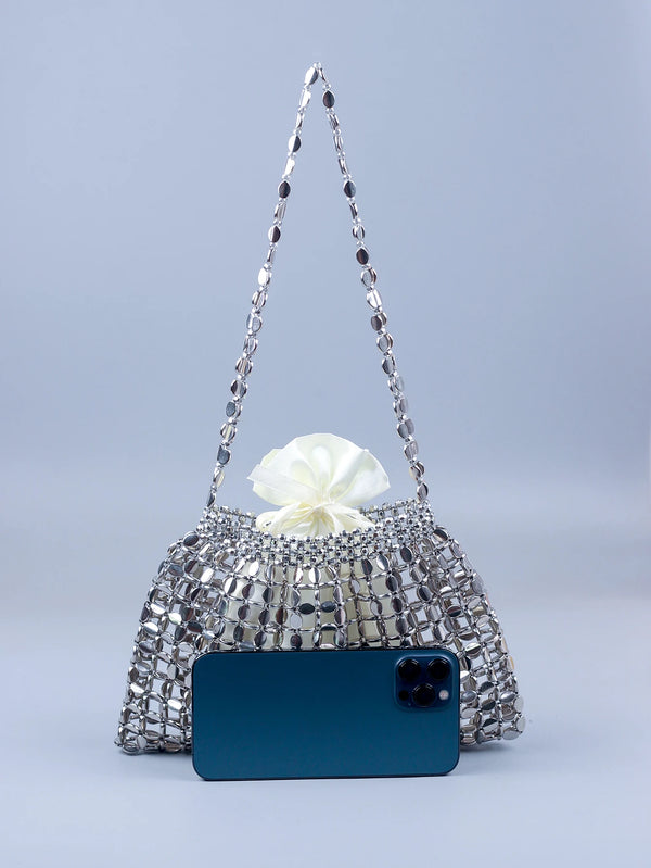 A handmade silver and gold beaded dumpling bag with a white bow, displayed above a dark blue smartphone.