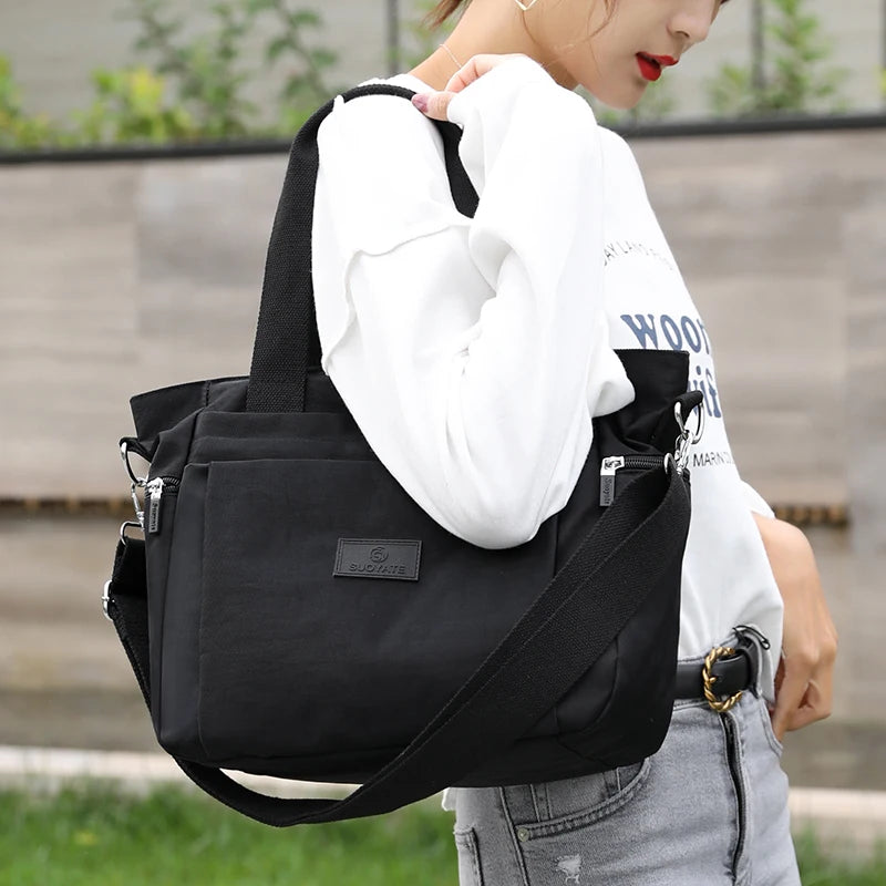 A woman holds a black durable nylon tote bag with a secure zipper closure against a blurred outdoor background.