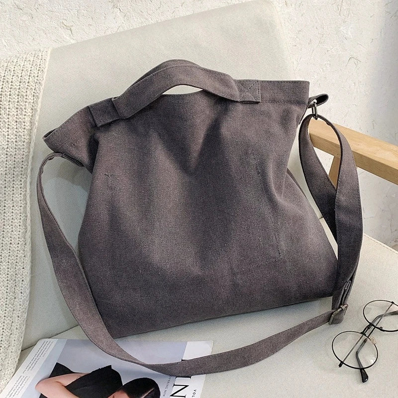 A gray canvas tote bag with a letter design is displayed on a white surface.