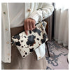 A hand holds a beige leopard print faux leather wrist bag with gold hardware against a light background.