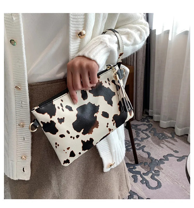 A hand holds a beige leopard print faux leather wrist bag with gold hardware against a light background.