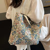 A light beige bohemian corduroy tote bag with a floral pattern is held by a person wearing a white blouse.