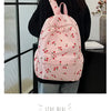 A pink corduroy fashion backpack with a pattern of red berries and leaves is shown being held by a person.