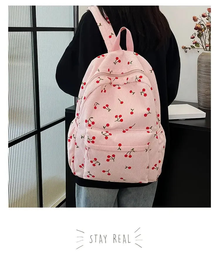 A pink corduroy fashion backpack with a pattern of red berries and leaves is shown being held by a person.