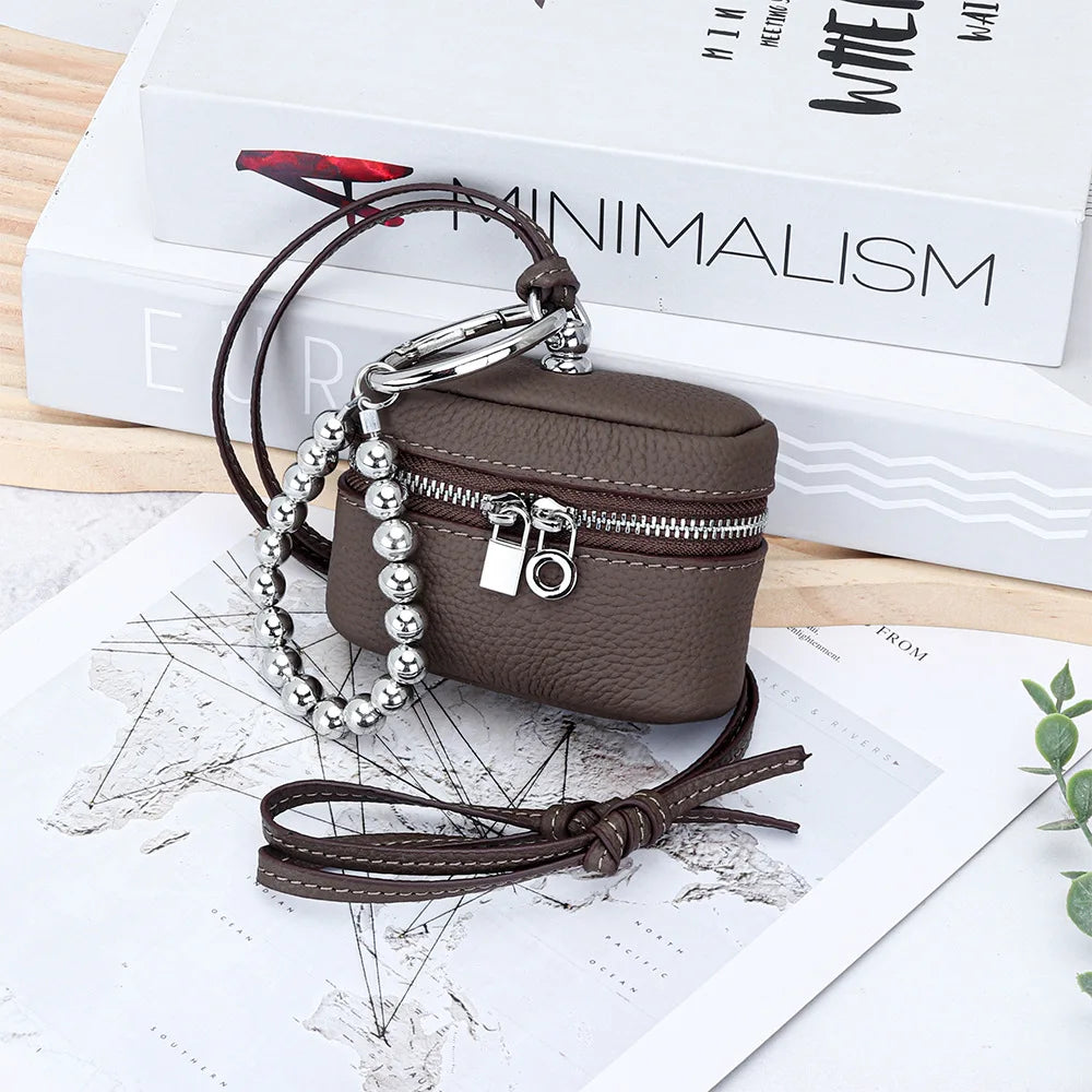 A dark brown leather coin purse with a silver chain and lanyard is displayed on a white background next to a book.